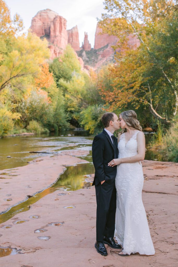 Couple kisses with the Oak Creek and the fall leaves and Cathedral Rock in the background.