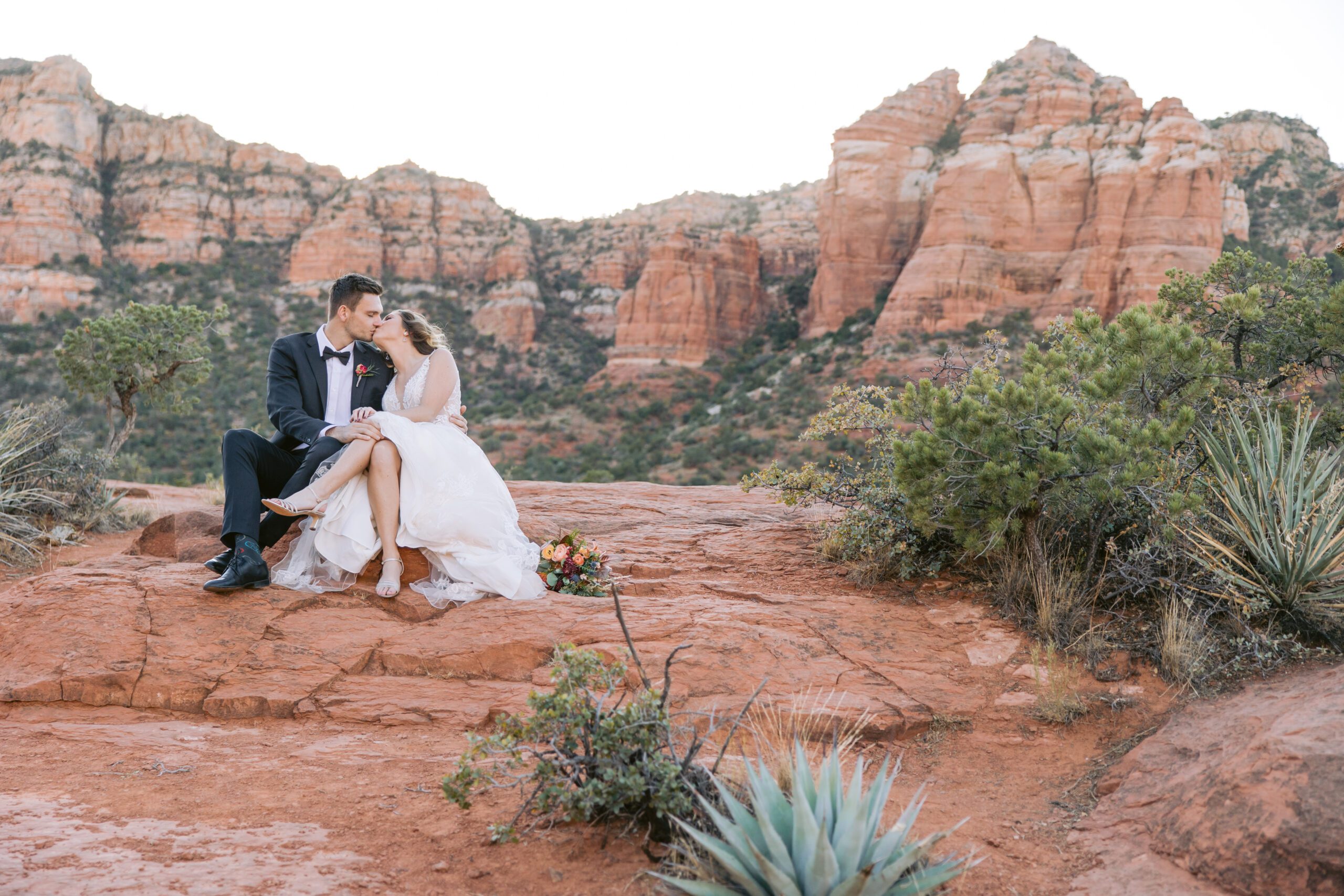 A couple sits on the red rocks and kisses during their Sedona elopement photography session.