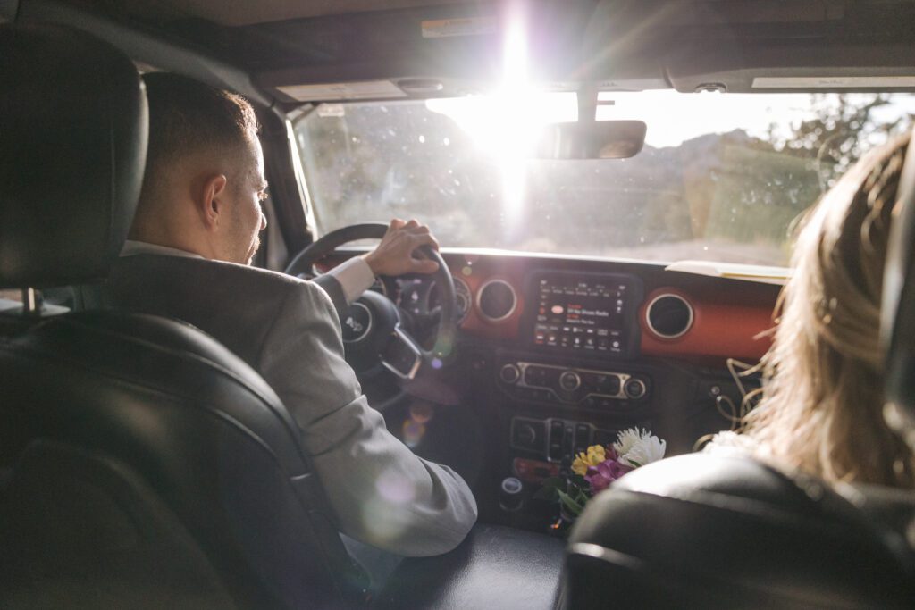 A groom in his suit drives a Jeep with his bride in the passenger's seat on a dirt road leading to Merry Go Round Rock where they will have their Sedona elopement.