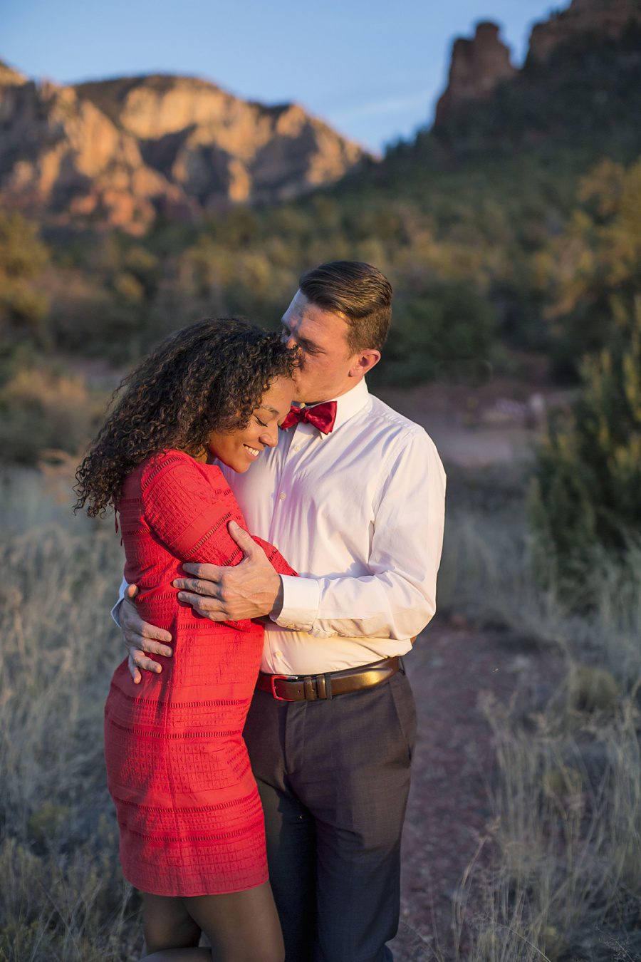 A man and woman embrace with the red rocks behind them