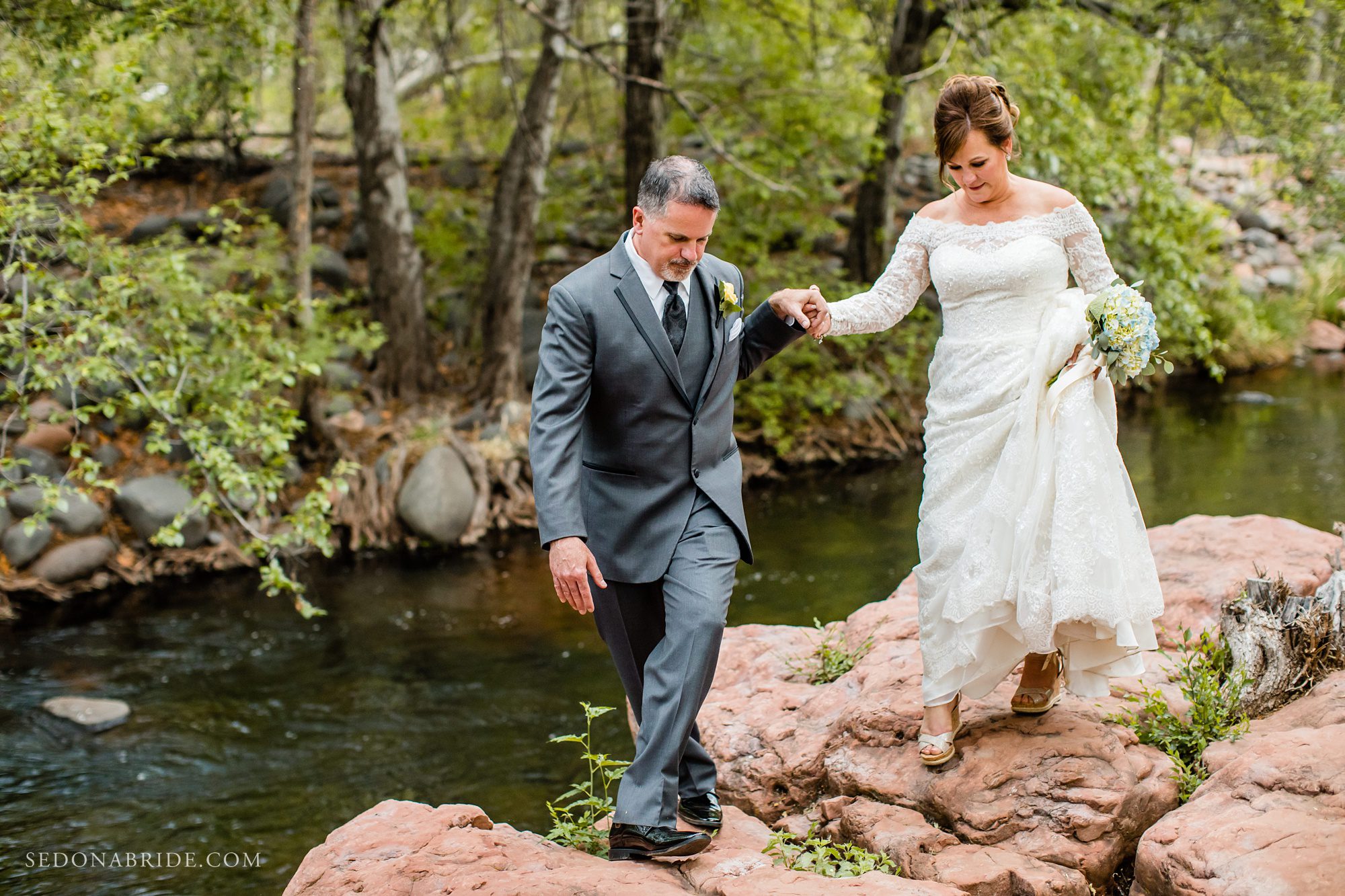 A groom helps his bride walk across the red rocks