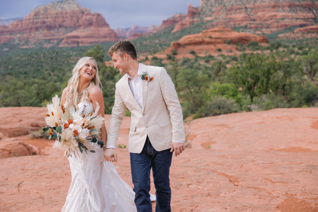 Bride and groom hold hands and walk on the red rocks during their elopement at Bell Rock.