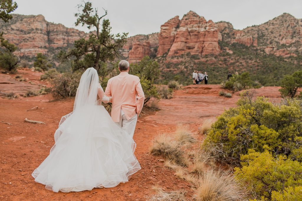 A wedding photo of a dad walking his daughter towards a wedding ceremony location on Bell Rock