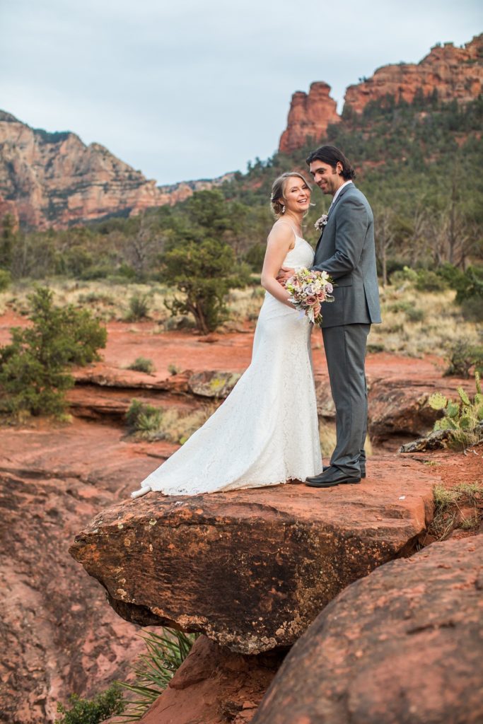 Bride and groom standing on a red rock ledge for their wedding photos at Schnebly Hill