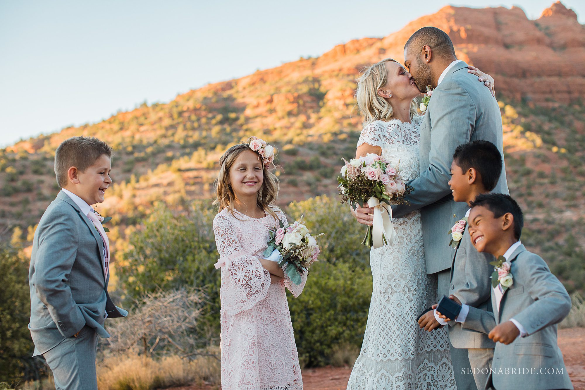 A bride and groom kiss while their kids smile during their elopement in Sedona