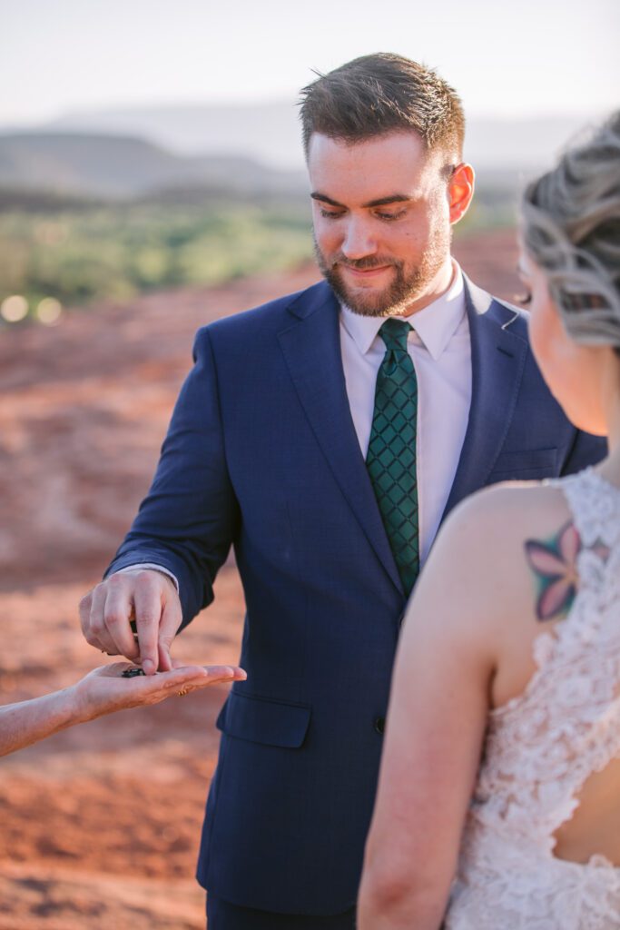 Groom reaches for a ring in the hands of an officiant during his wedding elopement at Secret Slick Rock.