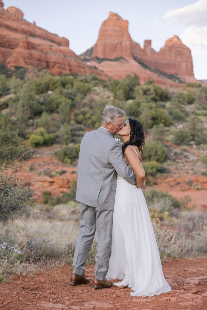 Groom and bride kiss and with the red rocks at Munds Wagon Trail in Sedona behind them.