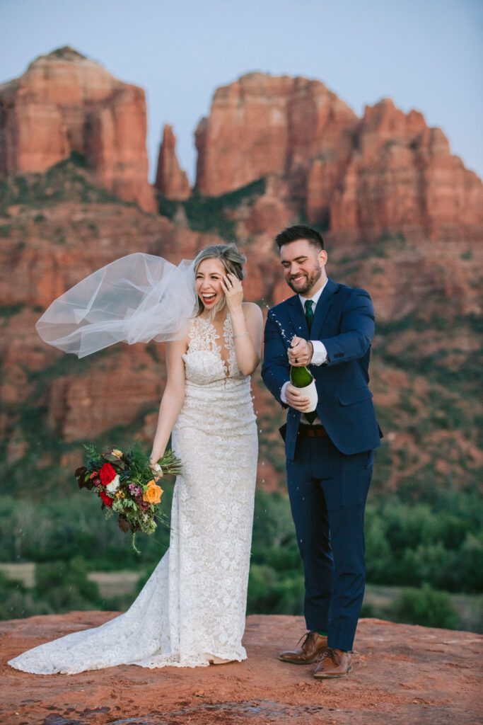 Bride laughs while the champagne bottle sprays champagne after the groom shakes the bottle.