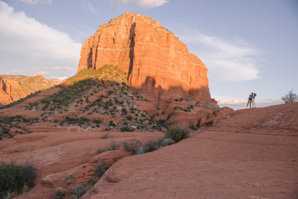 A couple kisses on the edge of the red rocks with the blue sky behind them and surrounded by red rocks while posing for their Sedona engagement photographer.