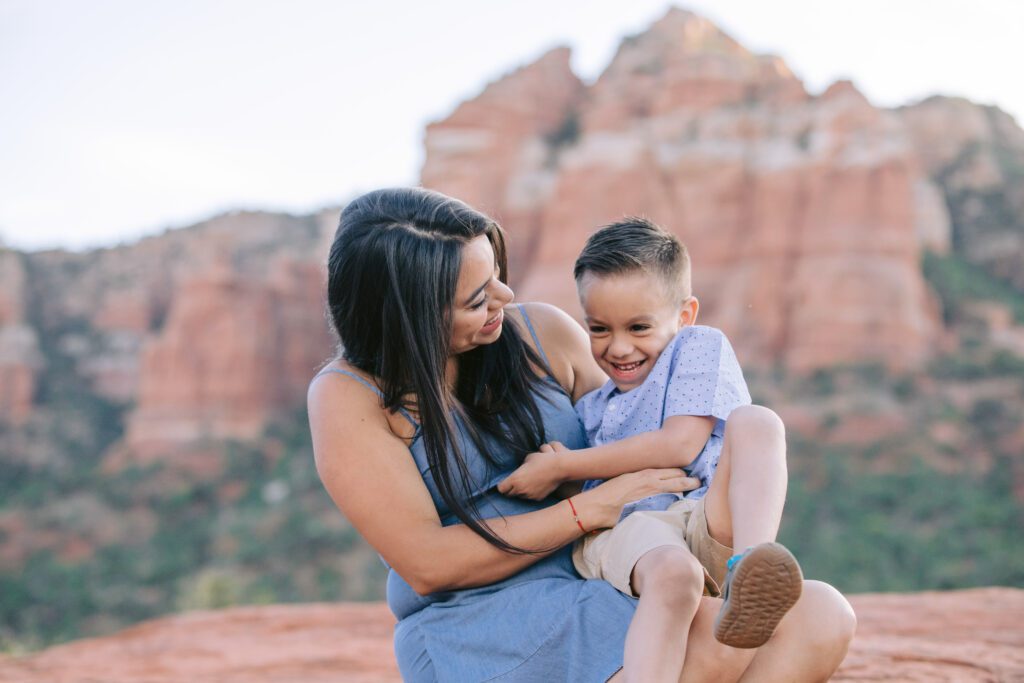 Mom with long black hair plays with her young son with tickles.