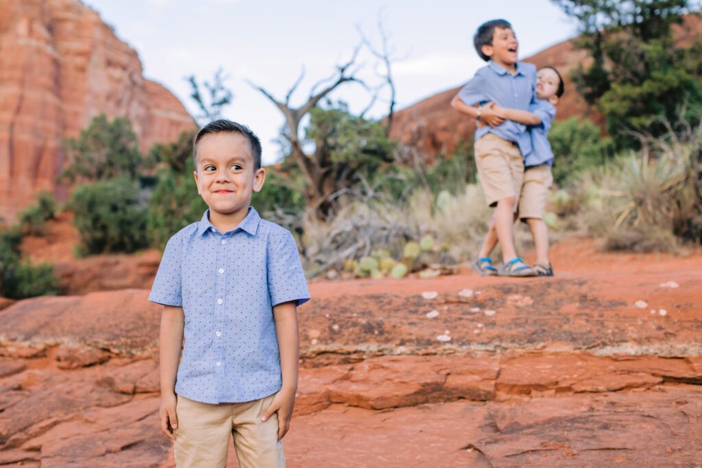 A boy makes a funny face while his brothers play in the background.