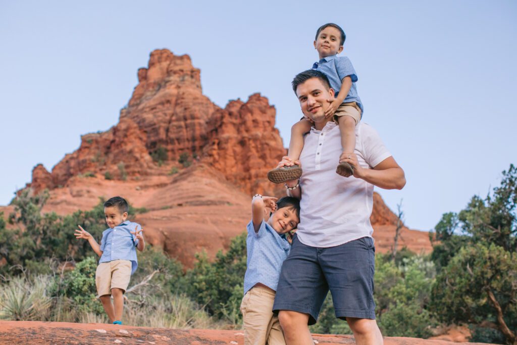 Dad holds his son on his shoulders while his other two sons play for their father, son, family photos.