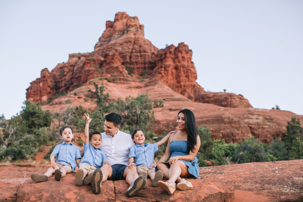A family wearing blue clothing for a family photo in Sedona sits and plays on the red rocks.