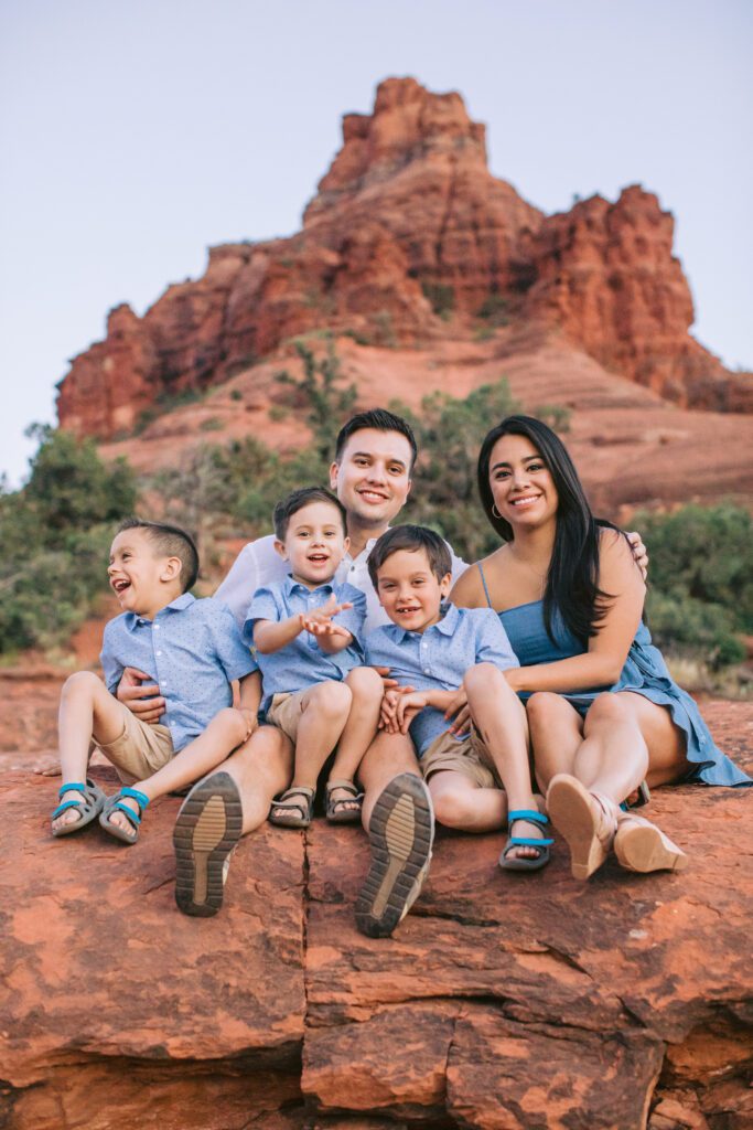 A family of five sit for a photo while the boys laugh. .