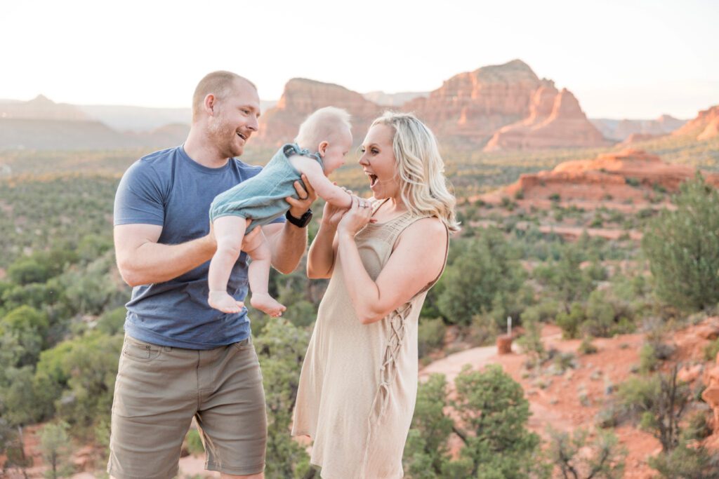A man in a blue shirt plays with his baby by swinging her in the air to her mom.