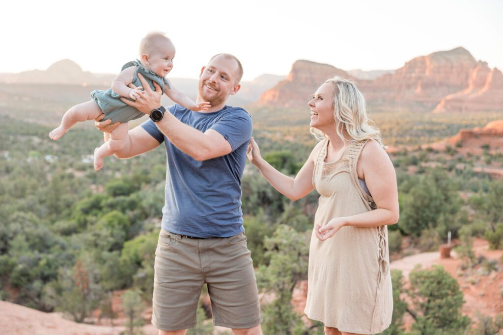 Dad swings his baby girl to her mom who is making fun faces at her baby for a family photo.