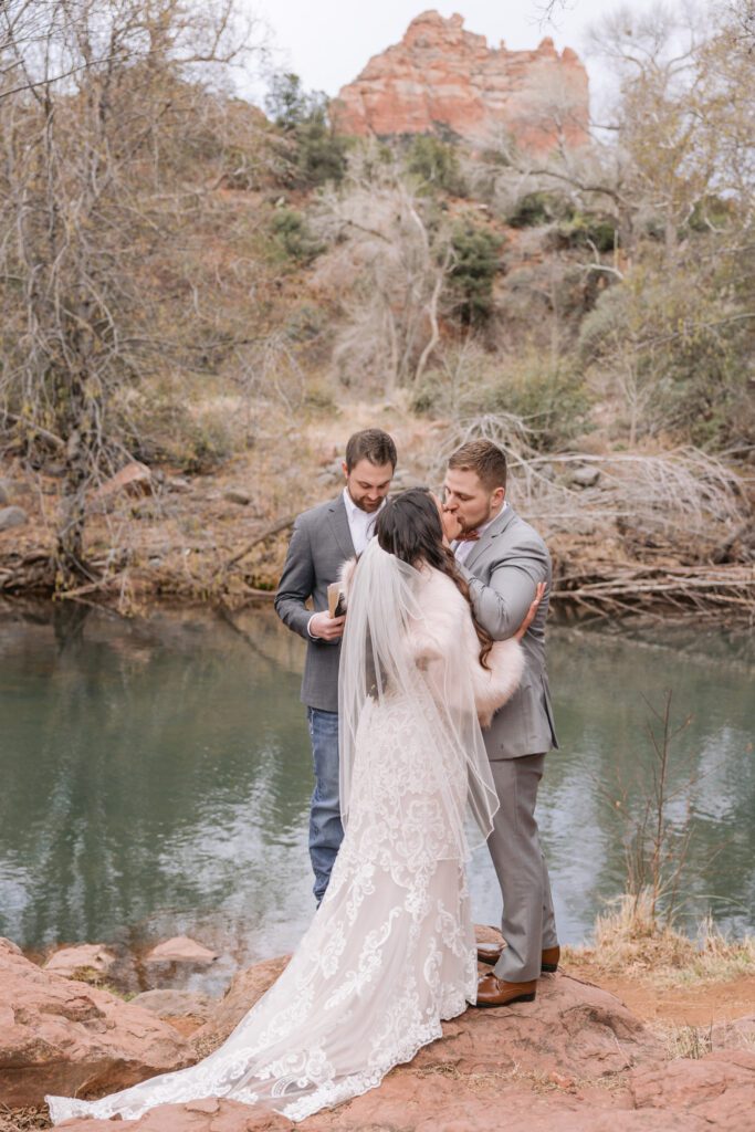 Bride and groom kiss next to the creek sharing their first kiss as husband and wife for their wedding ceremony.